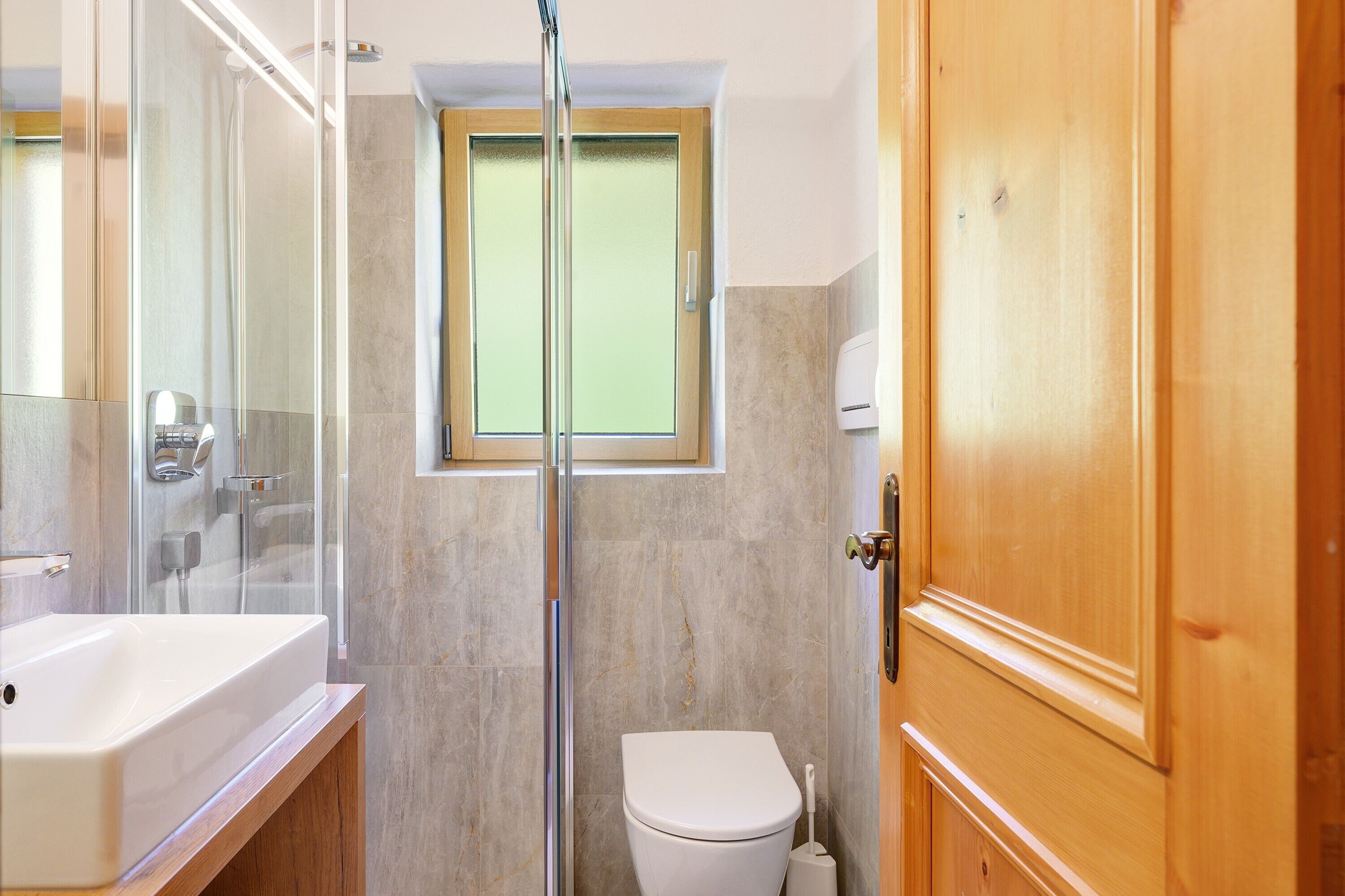 A bathroom with a glass shower enclosure, a toilet, and a sink.