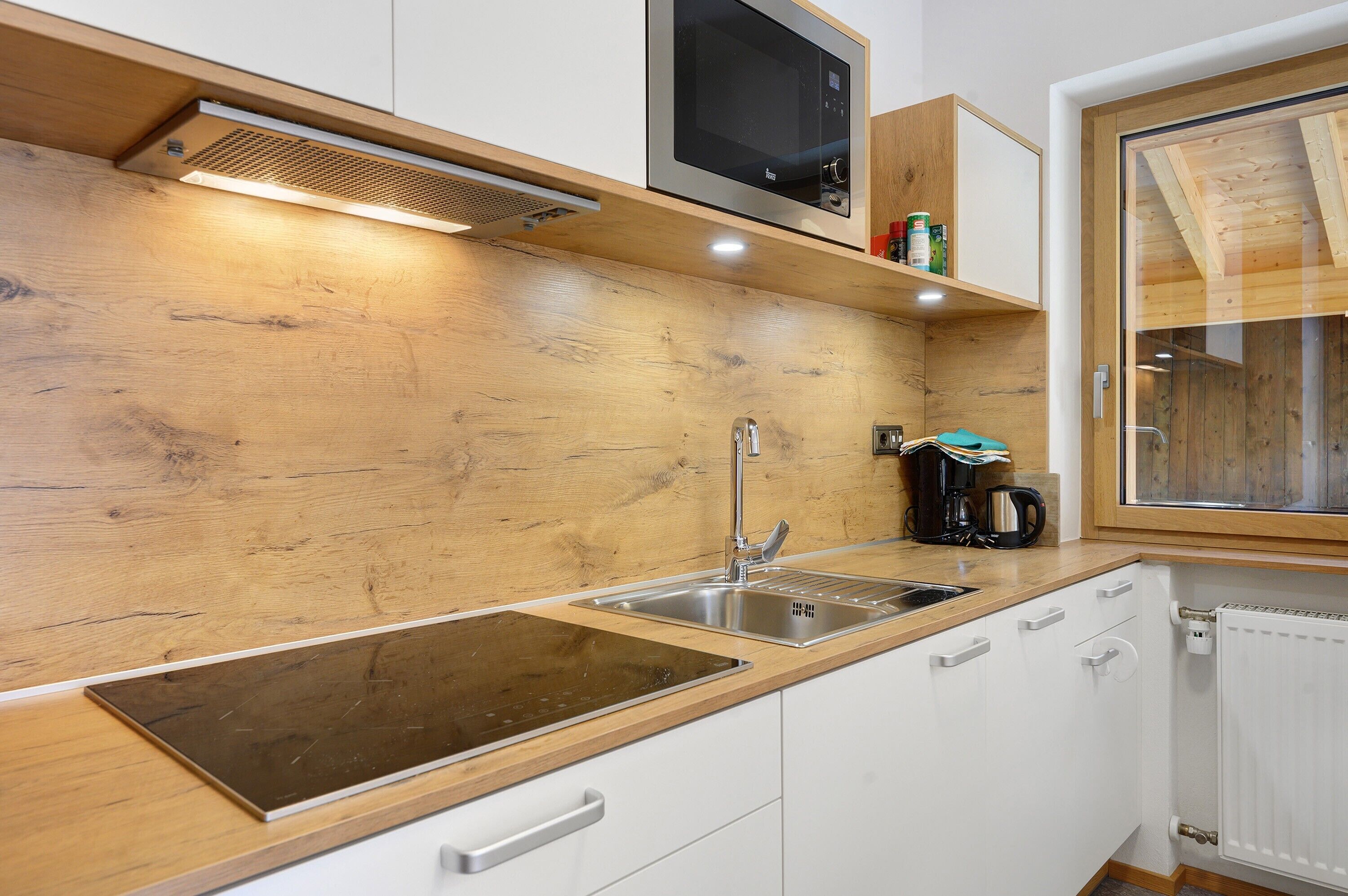 Una cocina moderna con armarios de madera, un lavamanos de acero inoxidable, un microondas y un ventanal con marcos de madera.