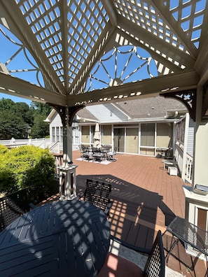 A covered outdoor patio with a pergola, a grill, and a table with chairs.