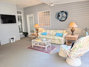A living room with a sofa, two side tables, a coffee table, a TV, and a decorative wall piece.