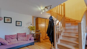 Een woonkamer met een houten trap, een roze bank en een houten kast.