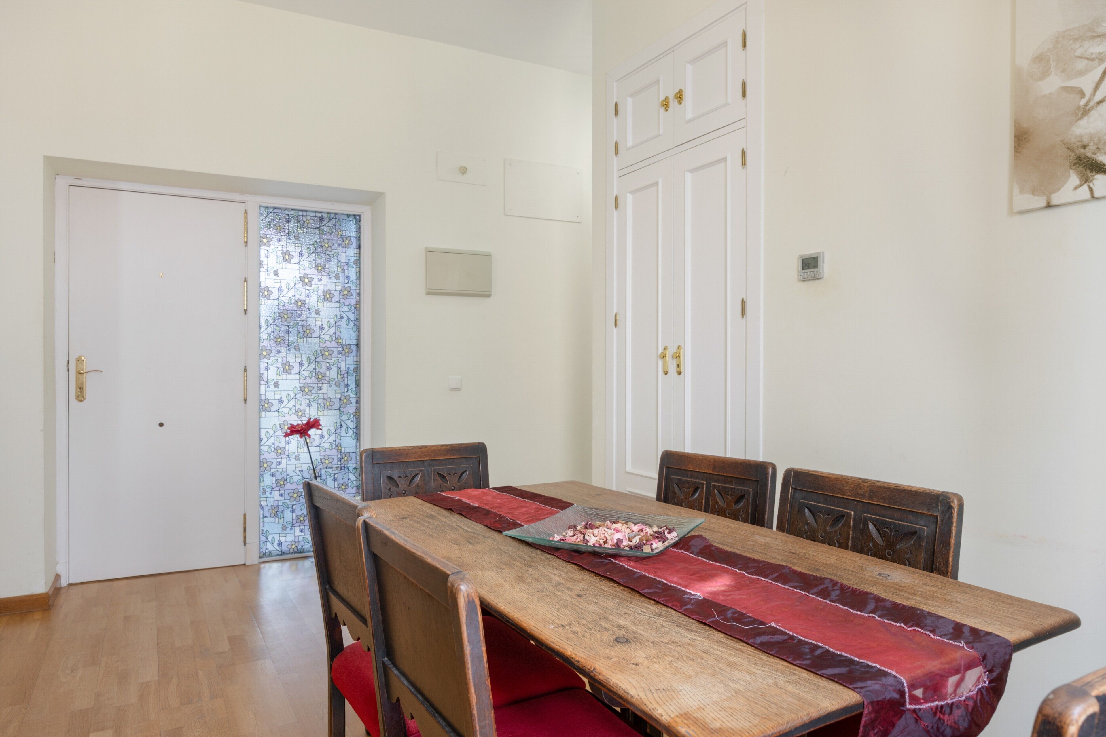 Un espace repas comprenant une table en bois, des chaises à revêtement rouge et un chemin de table en verre.