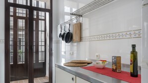 A kitchen with a sliding glass door, a hanging pot rack, a red mat, a bottle of olive oil, and a box of Calimero pasta. - Centrica Jerez Apartment with Shared Terrace, Wi-Fi, and Air Conditioning (Jerez de la Frontera)