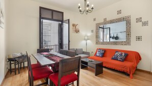 A dining area with a table and chairs, a sofa, a chandelier, and a wall with a mirror and decorative tiles. - Centrica Jerez Apartment with Shared Terrace, Wi-Fi, and Air Conditioning (Jerez de la Frontera)