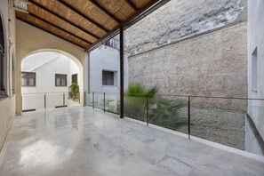 Un espacio interior amplio con suelo de mármol, barandilla de cristal y vistas a un edificio de fachada de piedra.