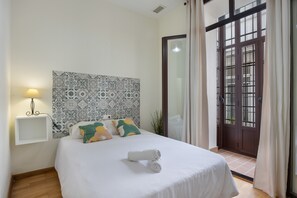 A hotel room with a bed, a wall-mounted shelf, a patterned headboard, and a door with glass panels.