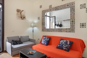A living room with a grey sofa, an orange sofa, a black coffee table, a mirror, and patterned tiles on the walls.