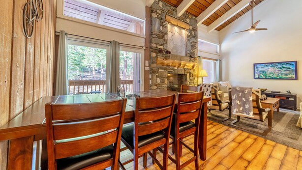 A dining area with a stone fireplace, wooden ceiling beams, and a view of the outdoors. - Updated Ski-Back Condo w/ Garage at Canyon Lodge (Mammoth Lakes)