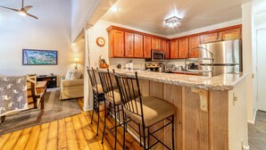 A kitchen with wooden cabinets, a stainless steel refrigerator, a microwave, and a bar area with stools. - Updated Ski-Back Condo w/ Garage at Canyon Lodge (Mammoth Lakes)