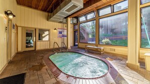 A spa area with a hot tub, wooden ceiling, and large windows overlooking a garden. - Updated Ski-Back Condo w/ Garage at Canyon Lodge (Mammoth Lakes)