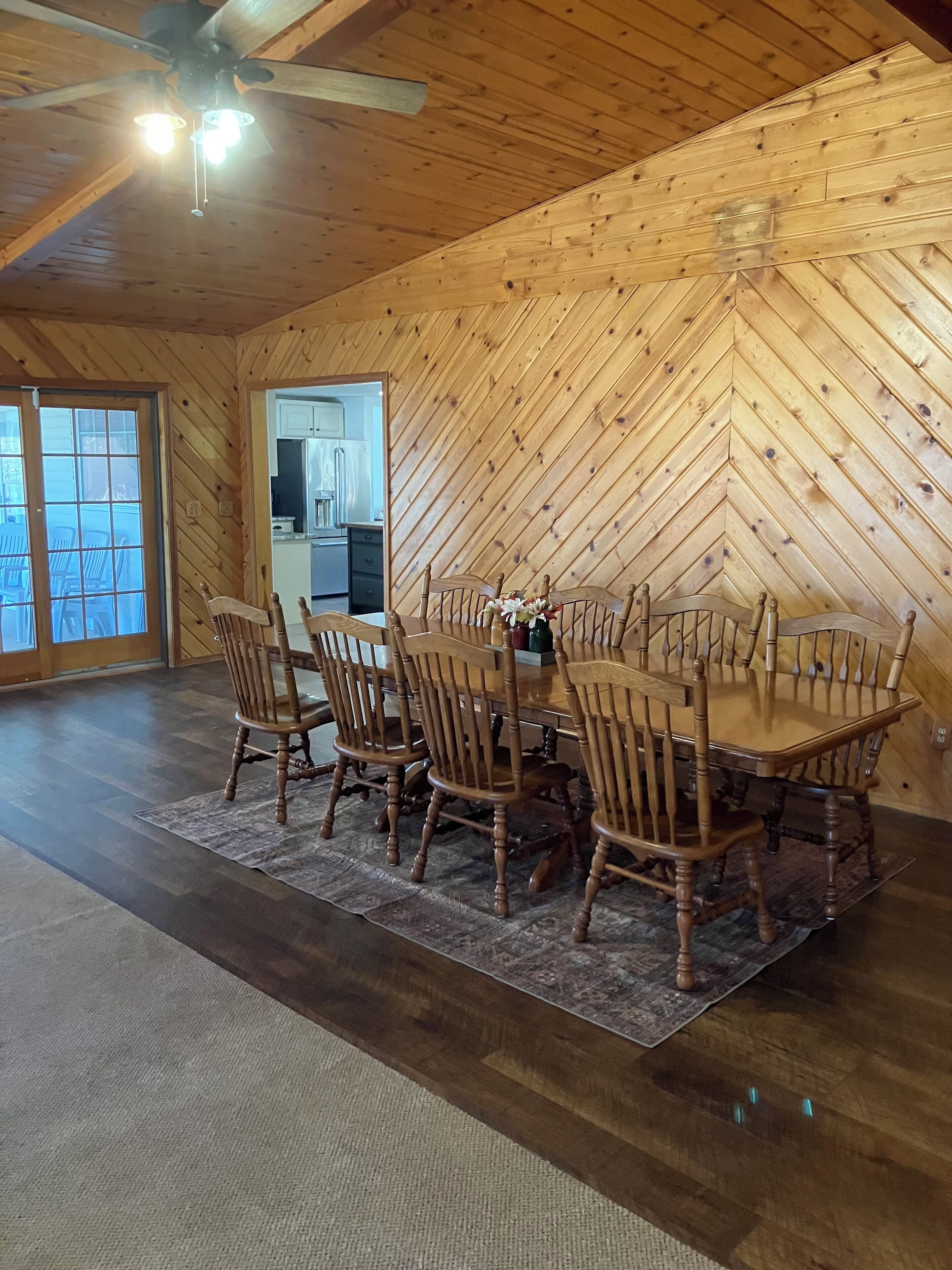A dining area with a wooden herringbone ceiling, a large wooden table, and six chairs.