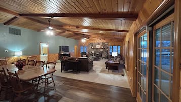 A spacious living area with a wooden ceiling, a stone fireplace, and a dining area with a table and chairs.