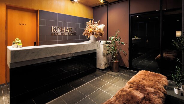 A reception area with a reception desk, a sign for 'KOHARU RESORT HOTEL & SITES', a potted plant, and a fur-covered bench.