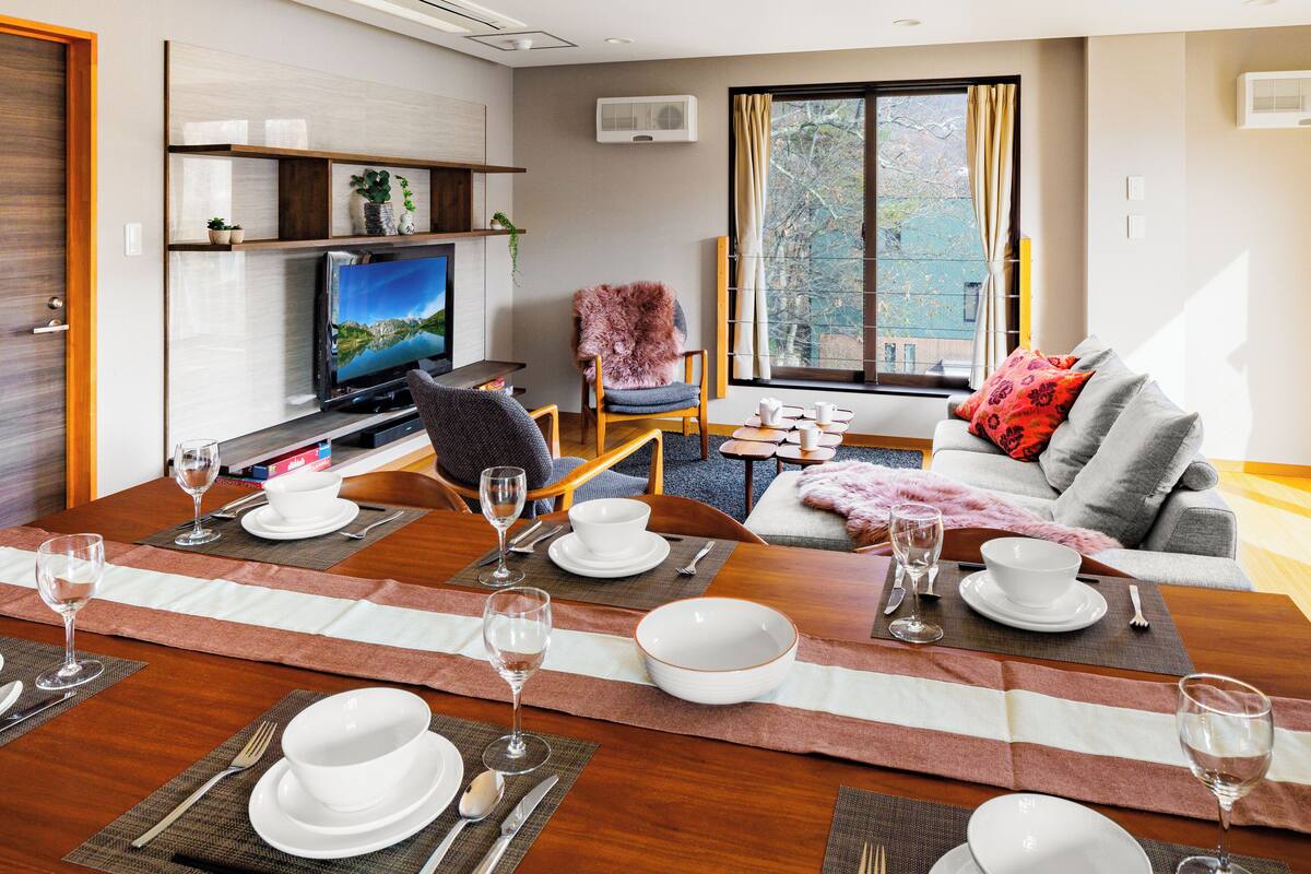 Een goed verlichte woonkamer met een televisie, zithoek en een eettafel voor twee personen.