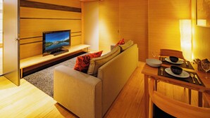 A modern living room with a sofa, a television, a dining table set with plates, bowls, and cutlery.