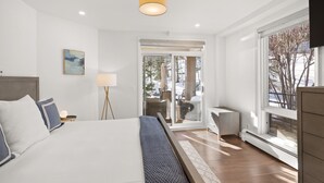 A modern bedroom with a large bed, a bedside table, a lamp, and a view of the outdoors through a sliding glass door. - Chamonix 30 | Snowmass Ski-In/Ski-Out Condo w/Shared Pool/Hot Tub/Private Washer/Dryer/Gym/WiFi (Snowmass Village)