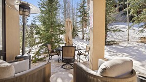 A covered outdoor seating area with wicker furniture, a table, and a heater. - Chamonix 30 | Snowmass Ski-In/Ski-Out Condo w/Shared Pool/Hot Tub/Private Washer/Dryer/Gym/WiFi (Snowmass Village)