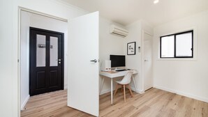 A modern, minimalist room with a wooden floor, white walls, a black door, a desk with a computer, and an air conditioning unit.