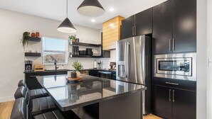 Une cuisine moderne avec des meubles de couleur noire, des appareils en acier inoxydable et un îlot central doté de sièges.