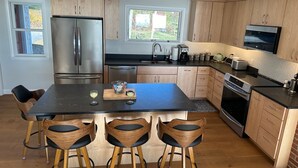 A modern kitchen with wooden cabinets, stainless steel appliances, a central island with bar stools, and a large window providing natural light. - Stunning Ocean Views, newly renovated cottage-close to preserves, trails, and Harpswell Beaches (Harpswell)