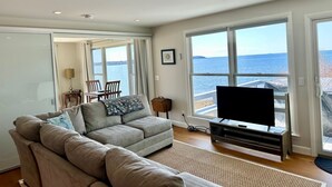 A living room with a sofa, a TV, and a large window with a view of the sea. - Stunning Ocean Views, newly renovated cottage-close to preserves, trails, and Harpswell Beaches (Harpswell)