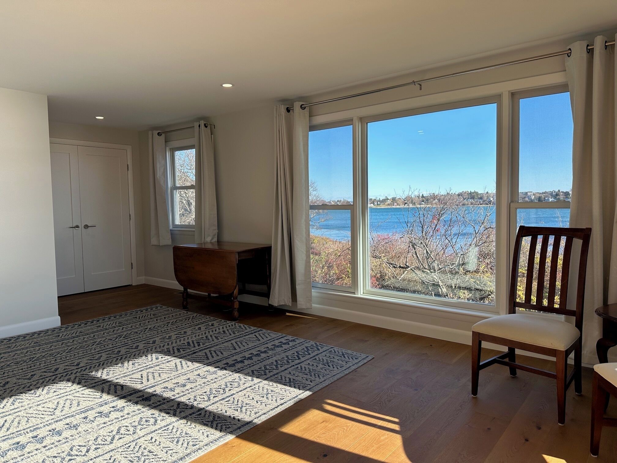 A spacious room with large windows offering a view of a body of water and trees.