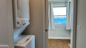 A laundry room with a washing machine and dryer, a window with a view of the sea, and a door leading to a room with a wooden floor. - Stunning Ocean Views, newly renovated cottage-close to preserves, trails, and Harpswell Beaches (Harpswell)