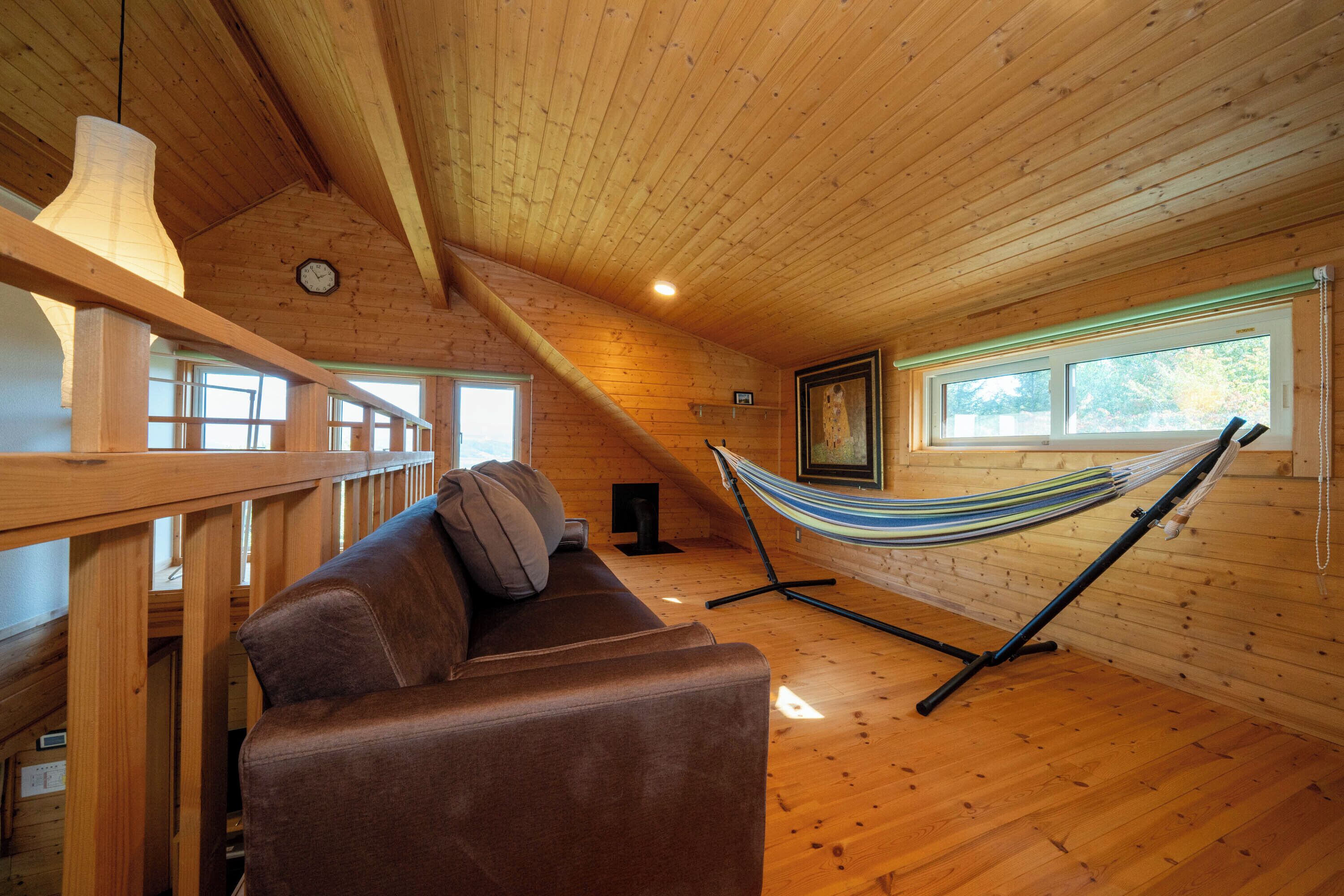 A wooden cabin interior with a hammock, a sofa, and a wooden railing.