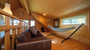 A wooden cabin interior with a hammock, a sofa, and a wooden railing.