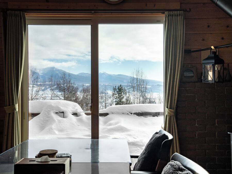 A room with a large window overlooking a snowy landscape with mountains.