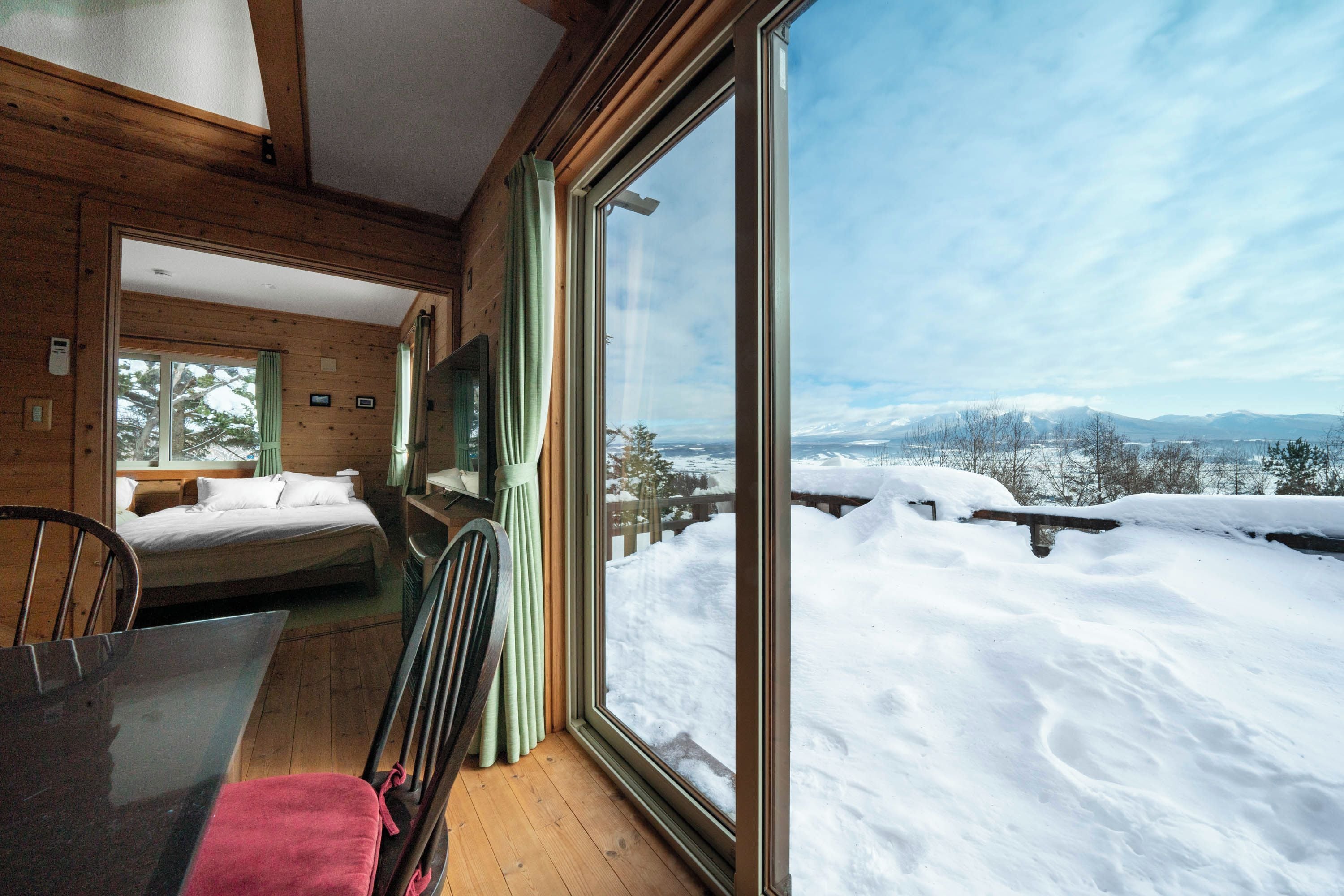 A wooden cabin with a large window overlooking a snowy landscape.