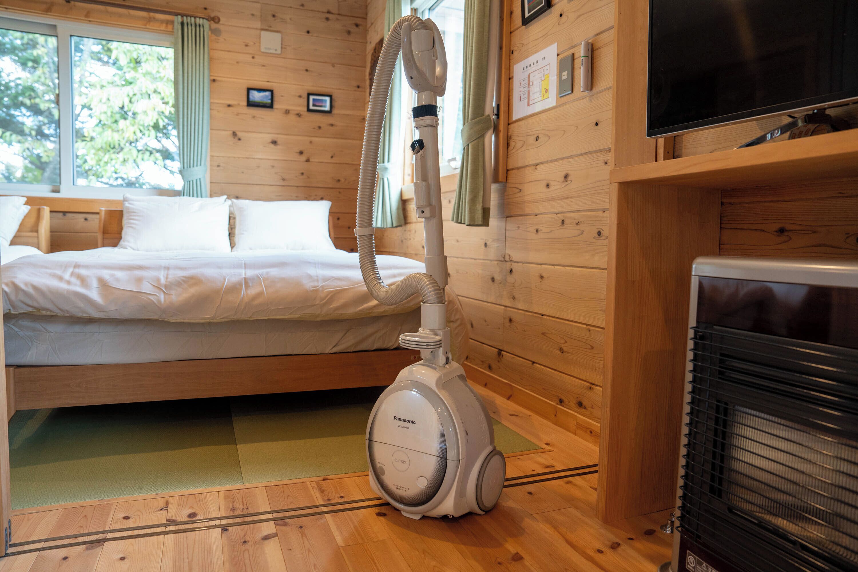 A room with a bed, a vacuum cleaner, a television, and a fireplace.