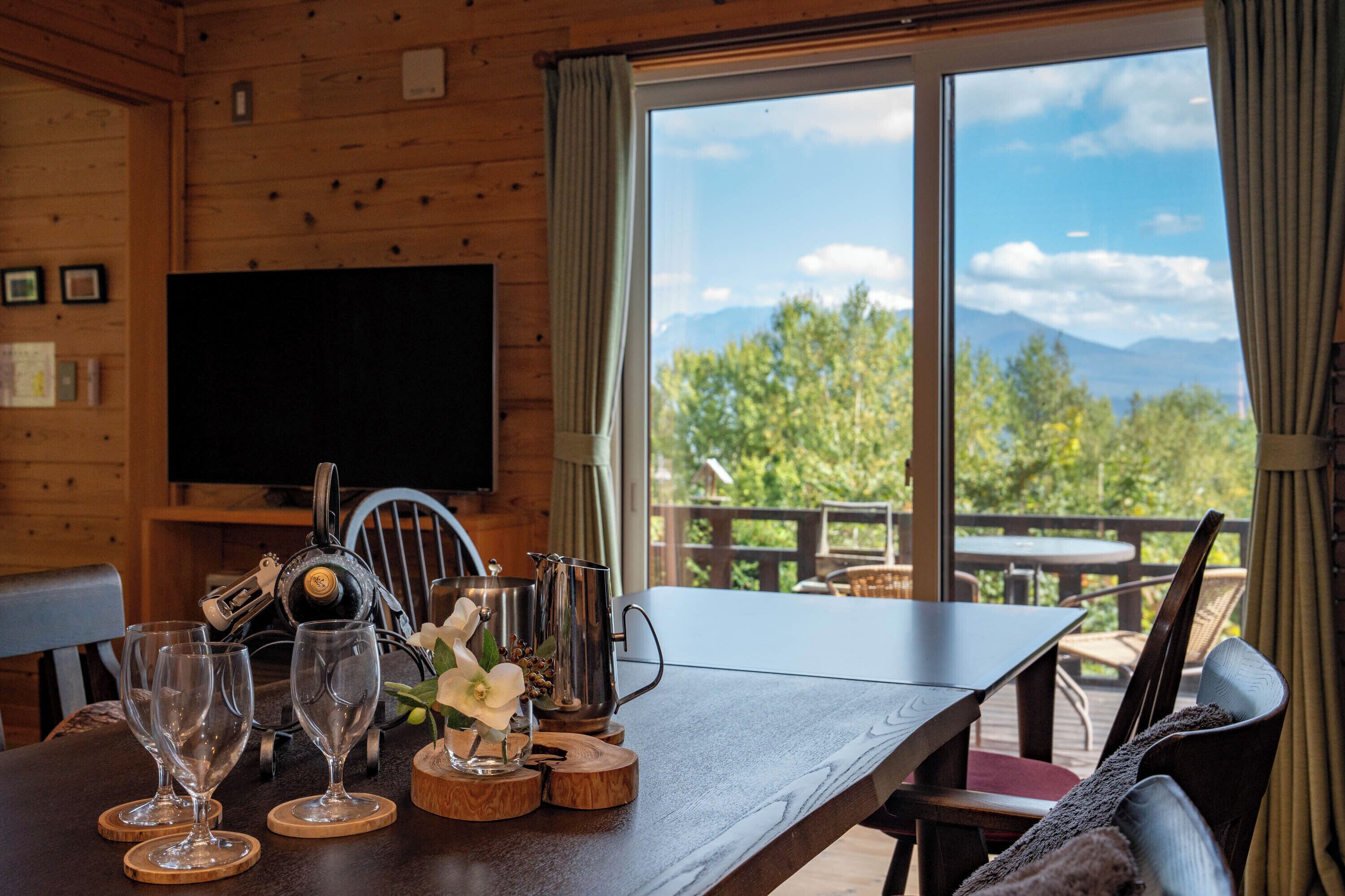 A wooden interior with a dining table, wine glasses, and a TV.