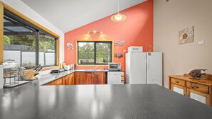 Eine Küche mit schwarzem Arbeitsplatz, Holzschränken, einem weißen Kühlschrank und einem Fenster mit Blick auf Bäume.