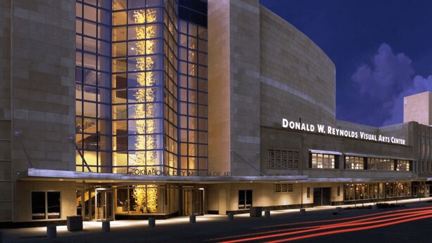 The exterior of the Donald W. Reynolds Visual Arts Center with a glass facade and illuminated interior. - 7BR Comfort Haven For 16 I Next to Tinker I EC (Midwest City)