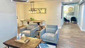 A modern living room with a dining area, featuring a wooden coffee table, light grey sofas, a dining table with chairs, and a ceiling fan. - 7BR Comfort Haven For 16 I Next to Tinker I EC (Midwest City)
