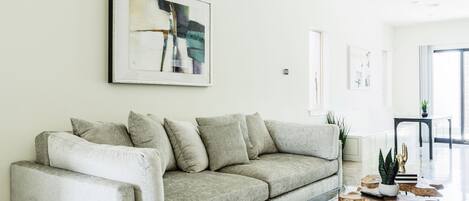 Ein modernes Wohnzimmer mit einem grauen Sofa, einem Couchtisch mit einer Pflanze und Kunstwerken an der Wand.