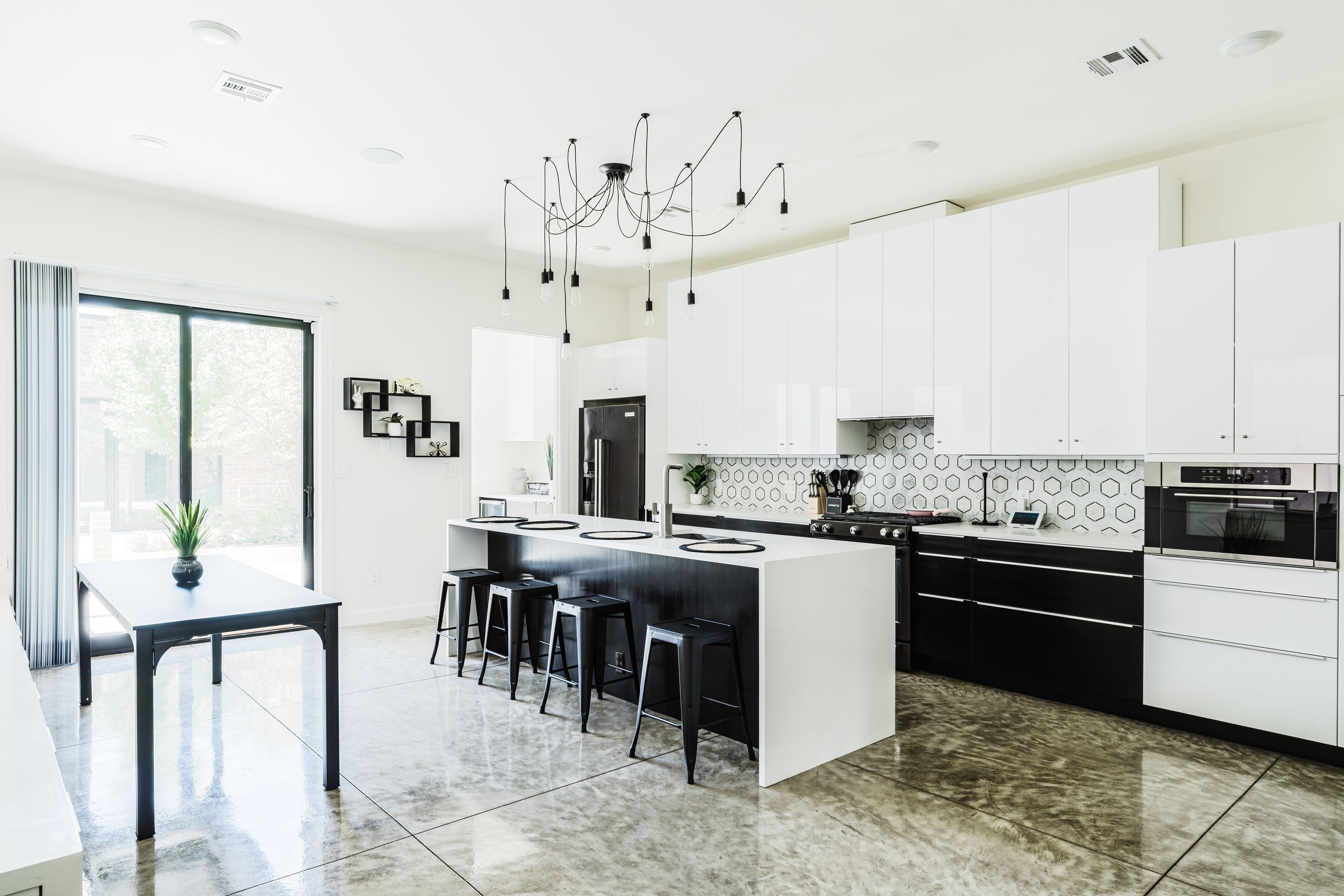 A modern kitchen with a central island, black bar stools, white cabinetry, and a chandelier.