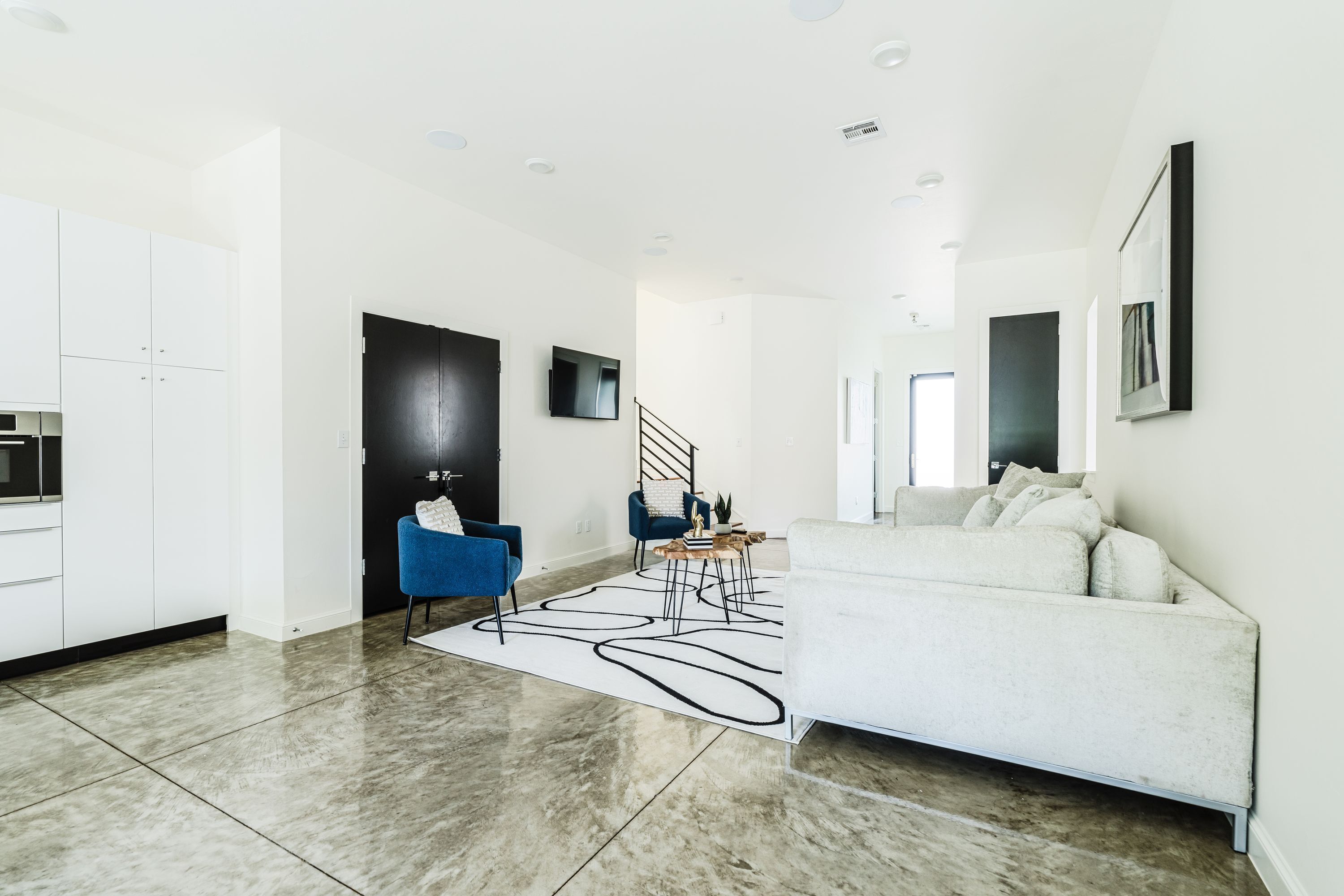 Un salon moderne avec un canapé, un fauteuil bleu, une table basse et un escalier menant à un autre niveau.