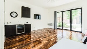 A spacious room with a wooden floor, a ceiling fan, a clock, a TV, and a sliding glass door leading to an outdoor area. - Cozy Getaway Perfect for 10 Prime Location NW6 (Oklahoma City)