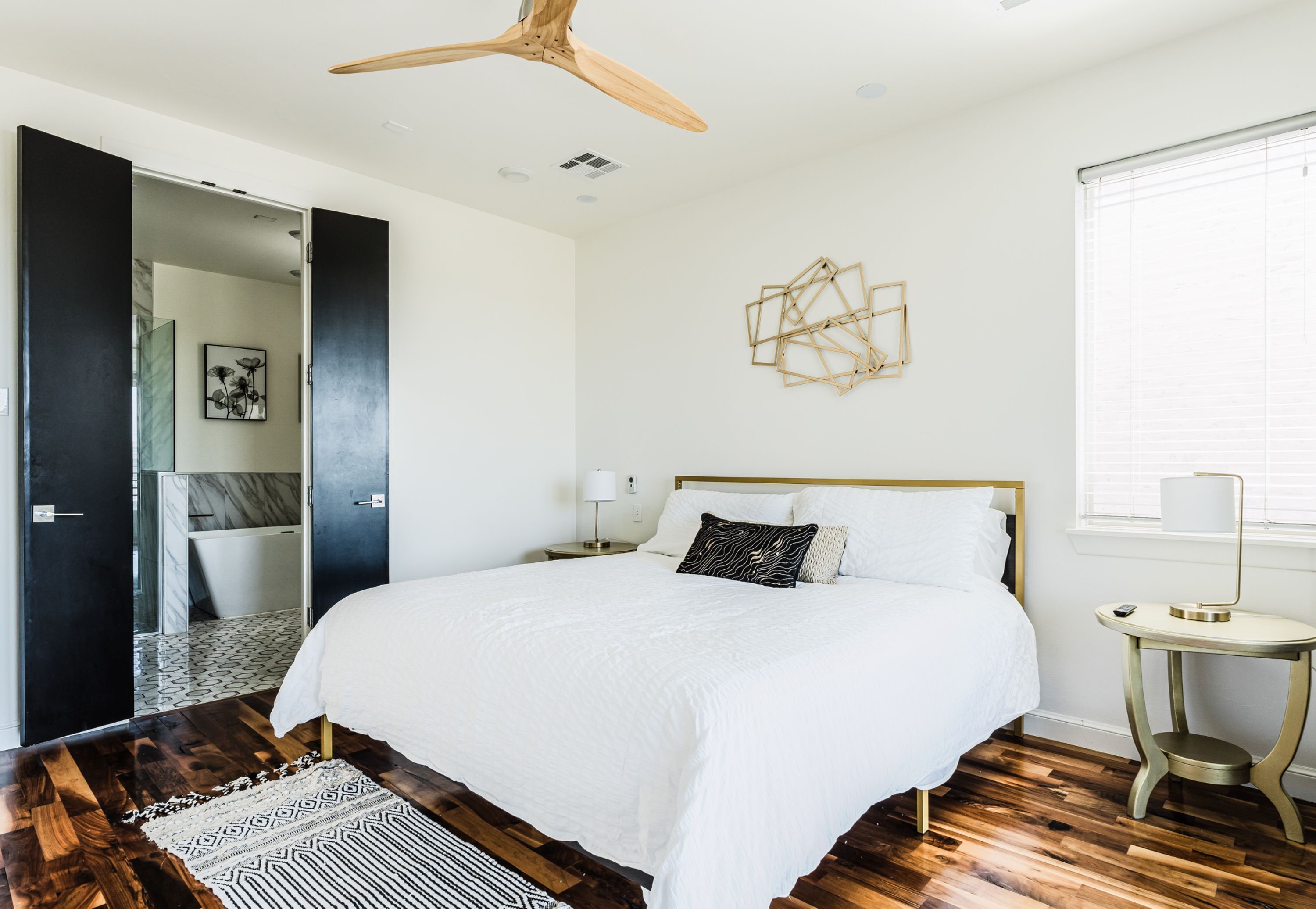 Un dormitorio moderno con una cama grande, suelo de madera y un ventilador de techo.