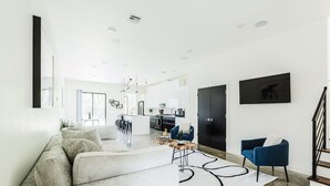 A modern living room with a sofa, a coffee table, and a blue armchair. There is a kitchen in the background with a dining area. - Cozy Getaway Perfect for 10 Prime Location NW6 (Oklahoma City)
