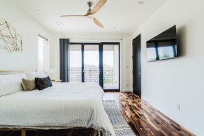 Een slaapkamer met een bed, een plafondventilator, een televisie, een groot raam en een deur naar een balkon.