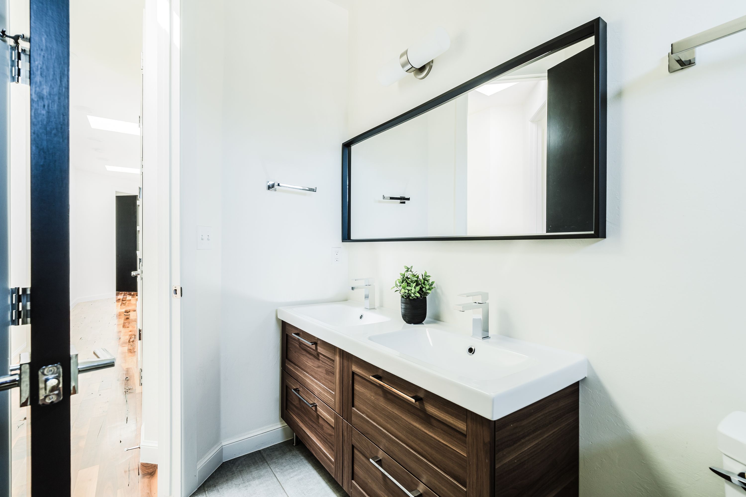 A modern bathroom with a white vanity, dark wood drawers, a large mirror, and a potted plant on the countertop.