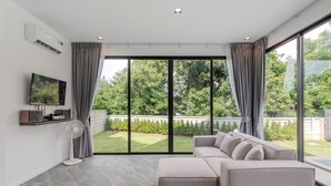 Ein modernes Wohnzimmer mit einem großen Ecksofa, einem flachbildfernseher an der Wand und einer großen Schiebeglasdoor, die in einen Garten führt.