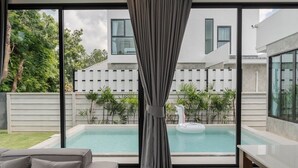 Ein modernes Wohnzimmer mit einem großen Fenster mit Blick auf einen Swimmingpool und ein weißes Gebäude.