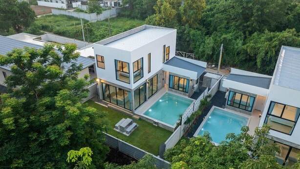 Ein modernes, zweistöckiges Haus mit großem Pool, umgeben von üppiger Vegetation.