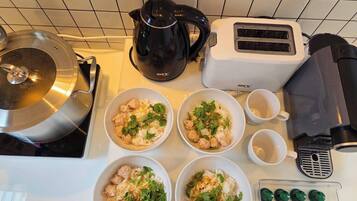 A kitchen counter with four bowls of rice topped with meat and herbs, a kettle, a toaster, and a coffee machine.
