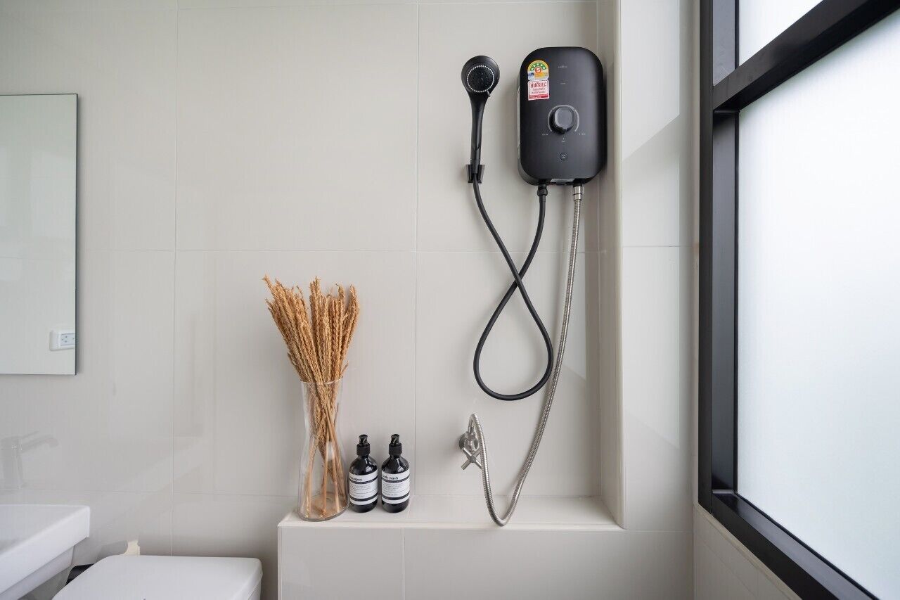 A bathroom with a shower, a toilet, and a sink. There are two bottles of shampoo and a vase with dried plants.