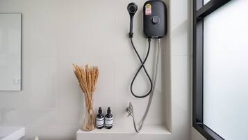 A bathroom with a shower, a toilet, and a sink. There are two bottles of shampoo and a vase with dried plants.